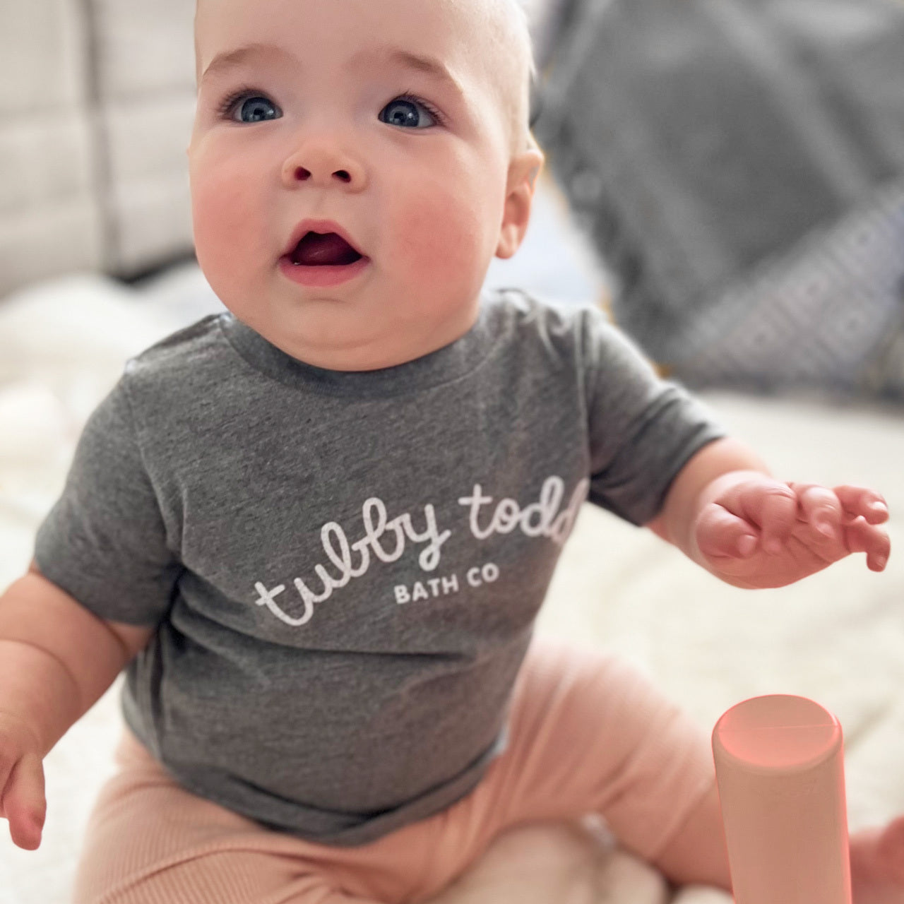 Baby wearing Tubby Todd grey baby tshirt while sitting up